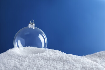 Transparent Christmas ball on snow against blue background, space for text