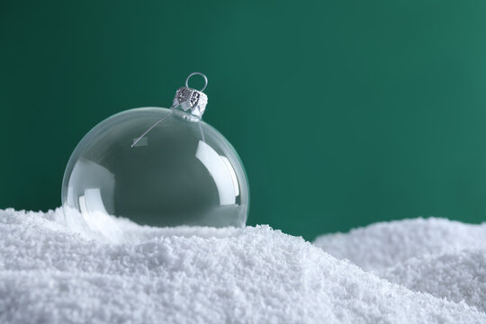 Transparent Christmas ball on snow against green background, space for text