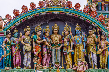 Fototapeta na wymiar Kadirampura, Karnataka, India - November 4, 2013: Sri Murugan Temple. Closeup of colorful statues together representing wedding of Murugan set on top facade under blue cloudscape.