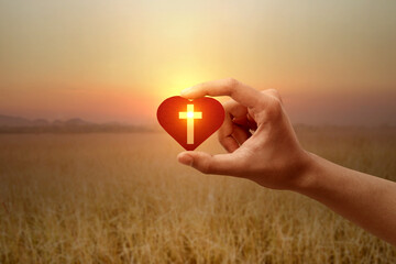 Human hand holding a red heart with a Christian cross