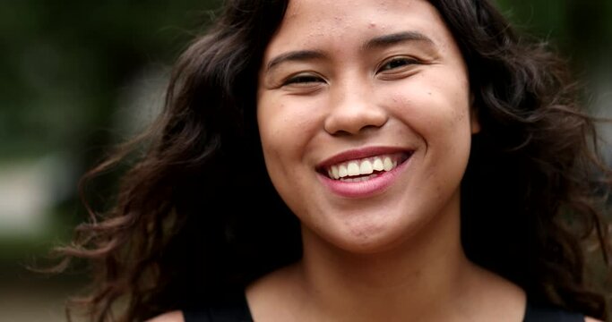 Happy hispanic woman standing outside at park smiling at camera. Mixed race latina girl portrait face, casual real people series
