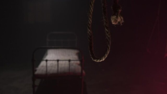 scary noose gallows for execution swings in dark against background of white metall bed in dark hospital or hangar sinister. Horror movie concept. bed with old mattress for corpse after hanging.