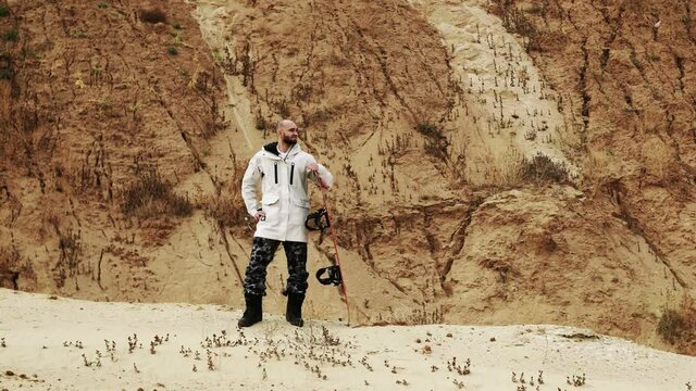 Handsome bald bearded man posing with sandboard in desert or sand quarry
