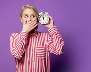 Beautiful woman in red striped shirt with alarm clock on purple background