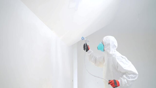 Airless Spray Painting. Worker painting the wall by airless spray gun with white color. Rear, back view. experienced man in equipment sprays acrylic white paint on surface with a mechanical air tool