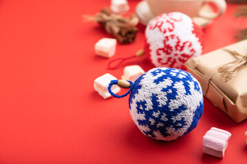 Christmas or New Year composition. Decorations, knitted balls, fir and spruce branches, cup of coffee, on a red background. Side view, copy space, selective focus.