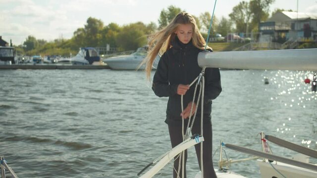 Long-haired beautiful girl stretches a rope through a boom, prepares for a sailing competition on a white yacht