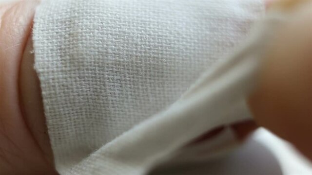 Remove the band-aid from the wound. Extreme close-up, real time, contains people, natural light, cotton weave
