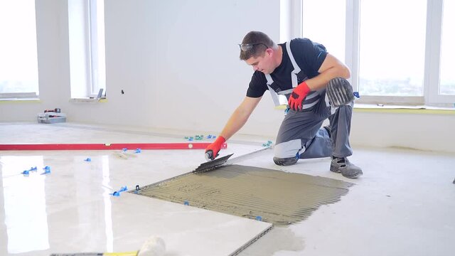 Construction repairs laying of a ceramic tile on a concrete floor with use of tool and glue mixes. Worker repairman Man builder master, notched trowel putting tiles adhesive mix with notched trowel