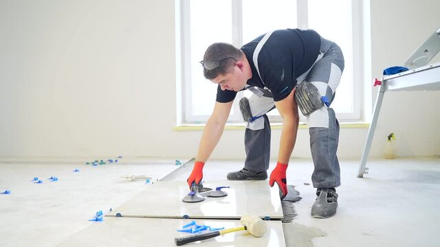industrial tiler Professional builder worker installing floor a large ceramic tile at repair renovation work. Man experienced repairman laying placing tile indoors house or apartment. Finishing works