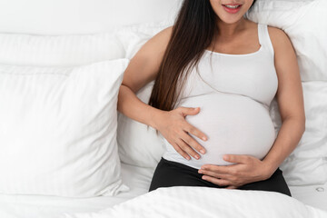 Asia happy pregnant woman is sitting on bed and and touching her belly. pregnancy, motherhood, people and expectation concept