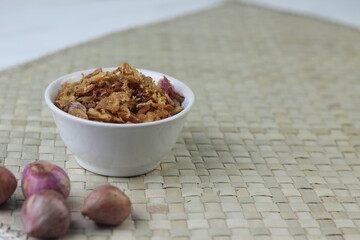 Bawang Merah Goreng or fried shallots, popular Indonesian food topping. Served on white ceramic bowl. Isolated background, copy space.