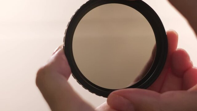 Photographic camera equipment filter isolated on white background. Concept. Female hands demonstrating the effect of polarizing filter for camera lens.