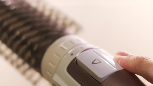 Close up of hot air rotating hair styler in female hands. Concept. Woman hands showing the work of air dryer isolated on white background, concept of beauty.