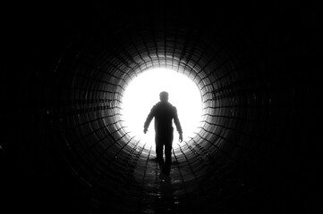 Silhouette of a man walking to the light at the end of a big tunnel. Concept of escape, exit,...