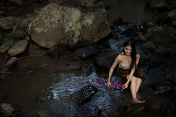 Portrait Asian young woman washing clothes at the stream.Beautiful Village women sitting and washing the clothes at the river.Countryside life style concept.