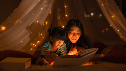 mom reading fairytale for daughter in kid tent before going to bed