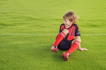 Little cute kid boy in red football uniform playing soccer, football on field, outdoors. Active child making sports with kids or father, Smiling happy boy having fun in summer