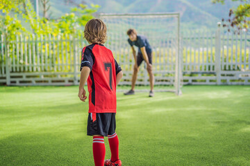 Obraz premium Little cute kid boy in red football uniform and his trainer or father playing soccer, football on field, outdoors. Active child making sports with kids or father, Smiling happy boy having fun in