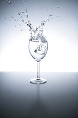 Beautiful splash in a wine glass with water drink and ice. Light background