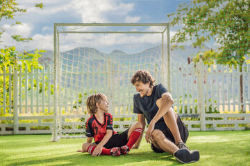 Little cute kid boy in red football uniform and his trainer or father playing soccer, football on...