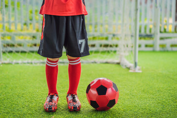 Obraz premium Little cute kid boy in red football uniform playing soccer, football on field, outdoors. Active child making sports with kids or father, Smiling happy boy having fun in summer