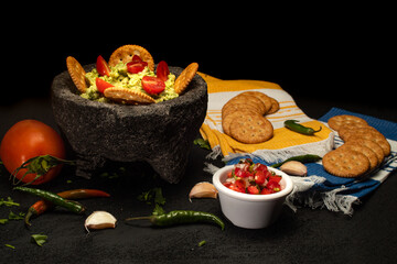 Guacamole served in a mexican molcajete (mortar) with crackers and pico de gallo (chopped tomato)