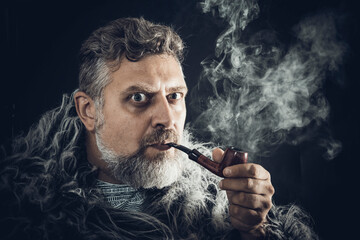 Solid bearded man in a fur mantle smoking pipe