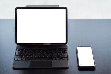 Digital tablet with blank screen on black table and smartphone in office.