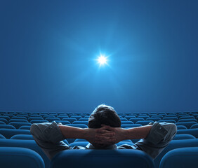 Empty blue cinema with person sitting in center and looking on bright star on screen