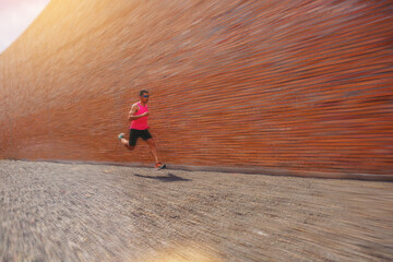 Runner start a race on a rock track with tall red brick wall as background with speed zoom blur.