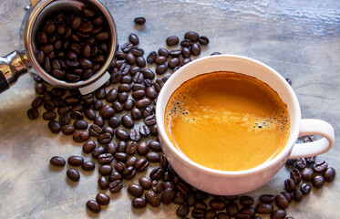  white cup of American coffee with a nice crema on top on a concrete table near a filter holder with arabica coffee beans. Focus on a cup of coffee