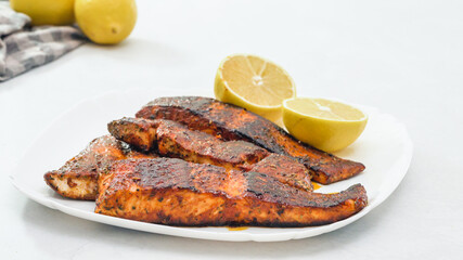 Smoked paprika roasted salmon pieces close up on a plate served with lemon