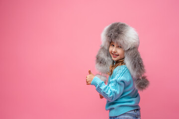 little girl in a white fur hat stands on pink background and shows the class