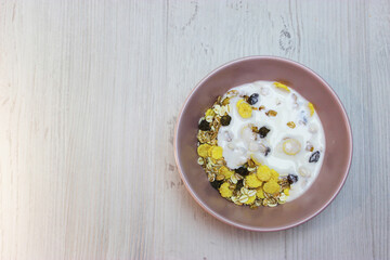 muesli with on a pink plate, top view. Muesli with fresh milk, yogurt or kefir. Muesli is made from oatmeal, a mixture of multi-grain flakes with dried fruits, nuts and sunflower seeds. on a white