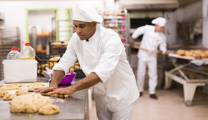 male baker in white uniform rolling out dough in kitchen
