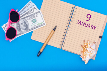 9 January. 9th day of January. Travel plan flat design with notepad written date, pen, glasses, money dollars and seashell on blue background. Winter month, day of the year, calendar concept