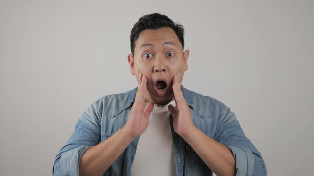 Portrait of young funny Asian man, gesturing shocked or surprised expression with mouth open
