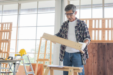 Senior asian old man carpenter wearing glasses and gloves protection building diy furniture in workshop