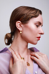Profile of young attractive woman with golden jewellery isolated on grey wall.