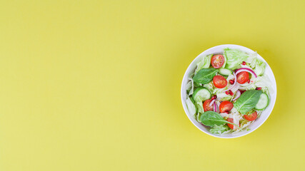 Fototapeta na wymiar fresh salad with cucumbers, tomato, onion, pomegranate, spinach and lettuce leaves on yellow background.