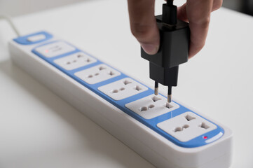 Hand holding Electric plug put on multiple socket. Electrical equipment, electrical wires and power strips in the house. Earth Hour saving electrical energy.