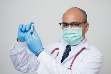 Asian bald Doctor in white coat, stethoscope, blue glove holding a bottle of.vaccine and look into camera isolated on white background.