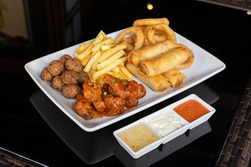Sharing platter with spring rolls, honey BBQ chicken drumsticks, onion rings, mini meatballs and French fries., 3 sauces