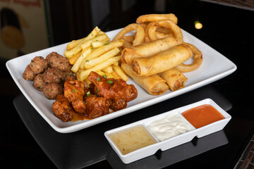 Sharing platter with spring rolls, honey BBQ chicken drumsticks, onion rings, mini meatballs and French fries., 3 sauces