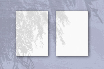2 vertical sheets of textured white paper on soft blue table background. Mockup overlay with the plant shadows. Natural light casts shadows from an exotic plant. Horizontal orientation