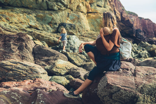 Mother with baby in sling watching her preschooler play on the rocks