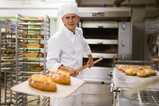 male baker with bread on baking shovel in kitchen