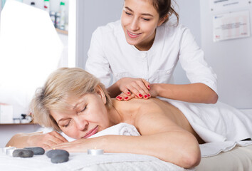 Obraz na płótnie Canvas Aged smiling woman having professional massage in spa salon
