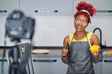 African american woman filming her blog broadcast about healthy food at home kitchen. She cuts a...